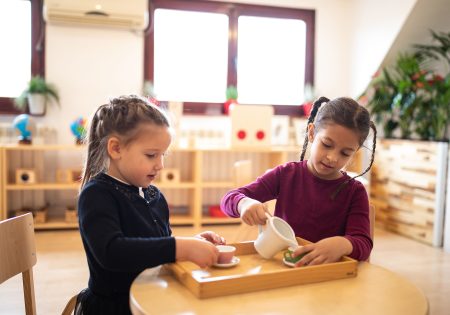 Two cute girls sitting at table and having a tea party in kindergarten